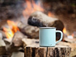 Eine Tasse steht auf einem Holzklotz vor einem Lagerfeuer