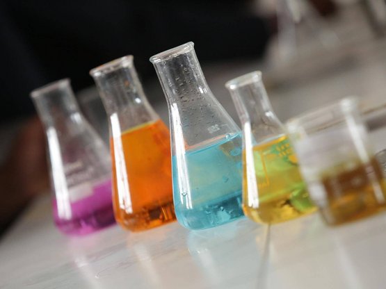 4 Zylingergefäße mit verschieden farbigen Flüssigkeiten stehen in einem Labor