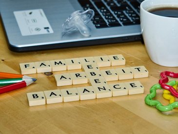 Scrabble Buchstaben liegen vor einem Laptop auf dem Tisch und formen die Worte Familie, Leben, Arbeit, Balance